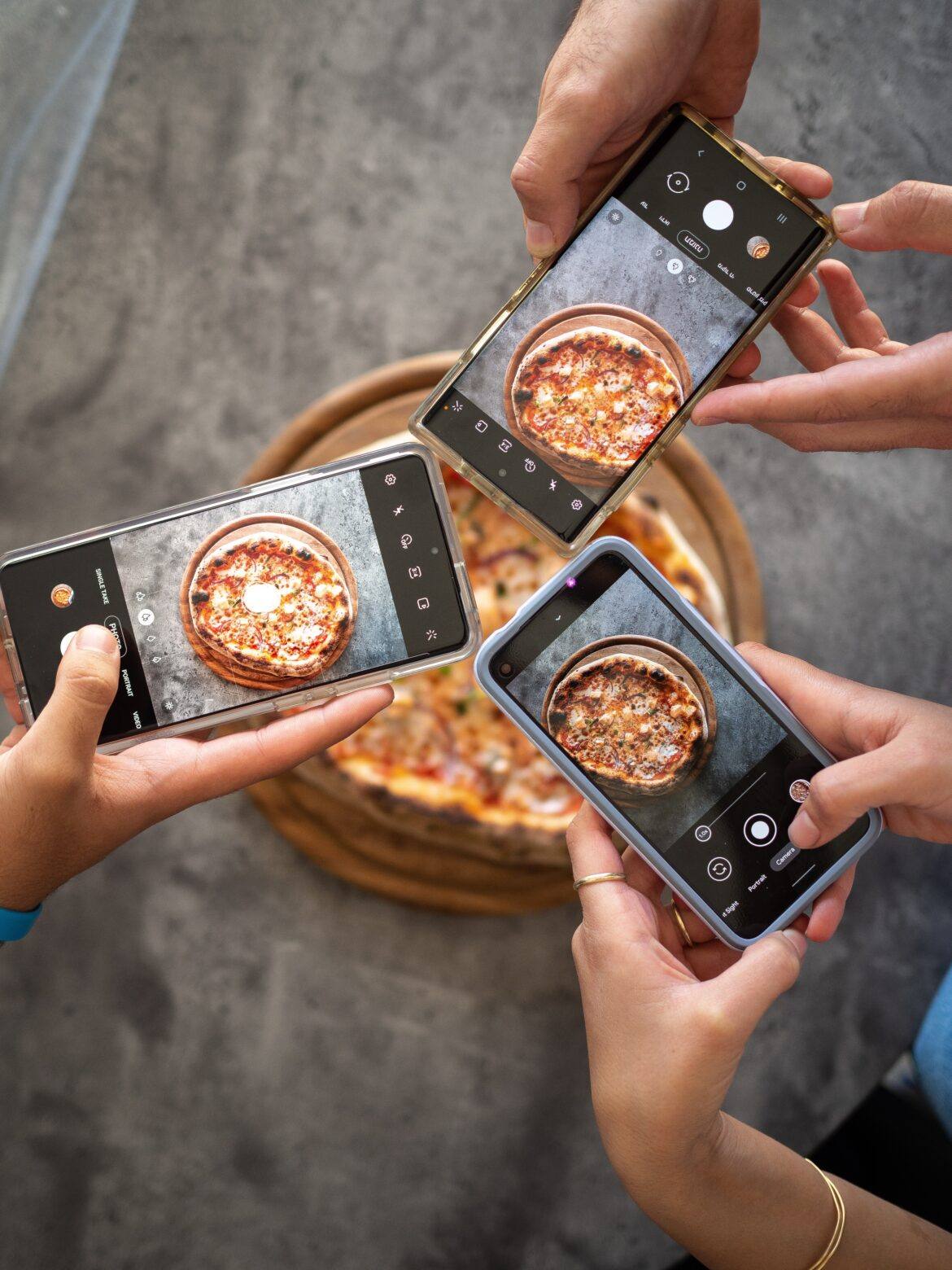 yoav-aziz-1uQQrwzjKms-unsplash 3 people snapping a picture of a pizza