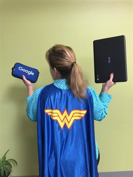 The backside of my colleague Diana wearing a Wonder Woman cape while holding a google adapter bag and computer. 