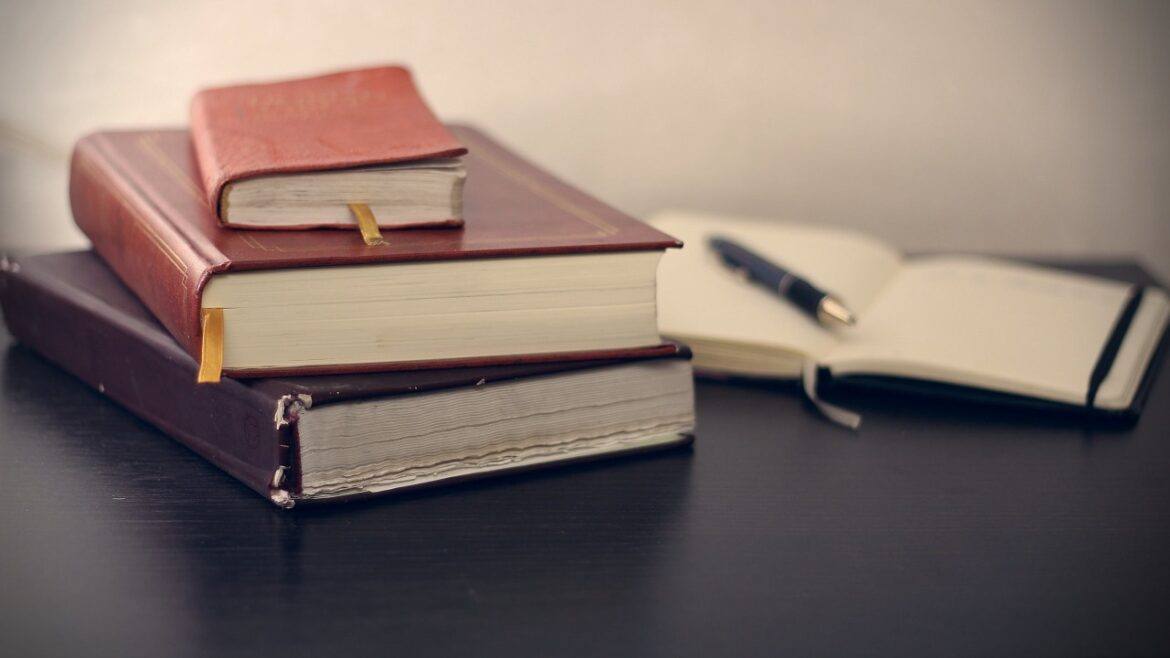 stack of books with pen and paper reading writing