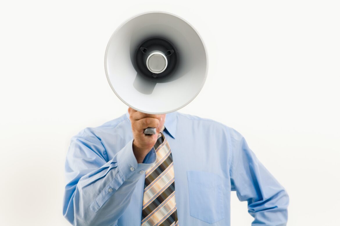 pexels-pressmaster-3851254 a man in a tie speaks through a megaphone