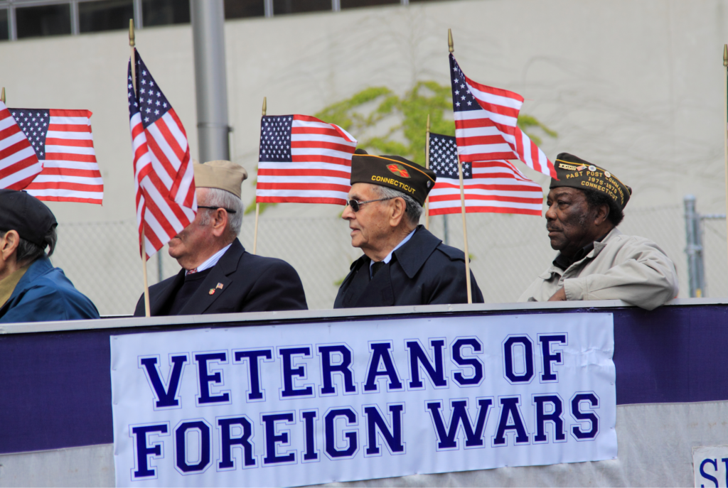 Veterans in uniform with American flags on a Veterans of Foreign Wars float in a Veterans Day Parade.