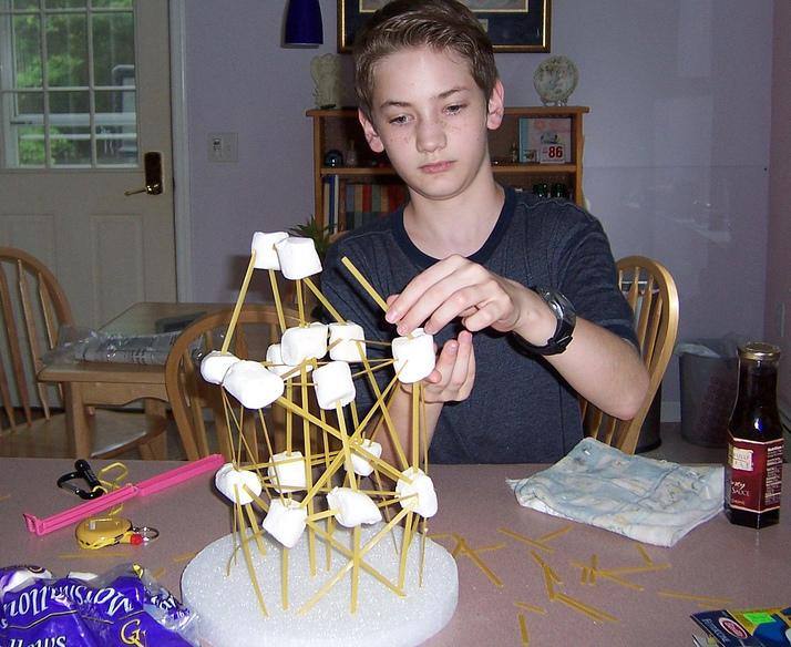 A student building a tower using marshmallows and wooden sticks.