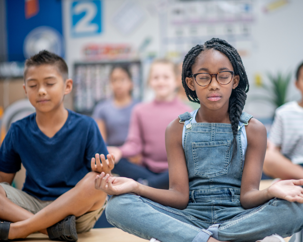 Students are seated with legs crossed and practicing mindful breathing in the classroom.