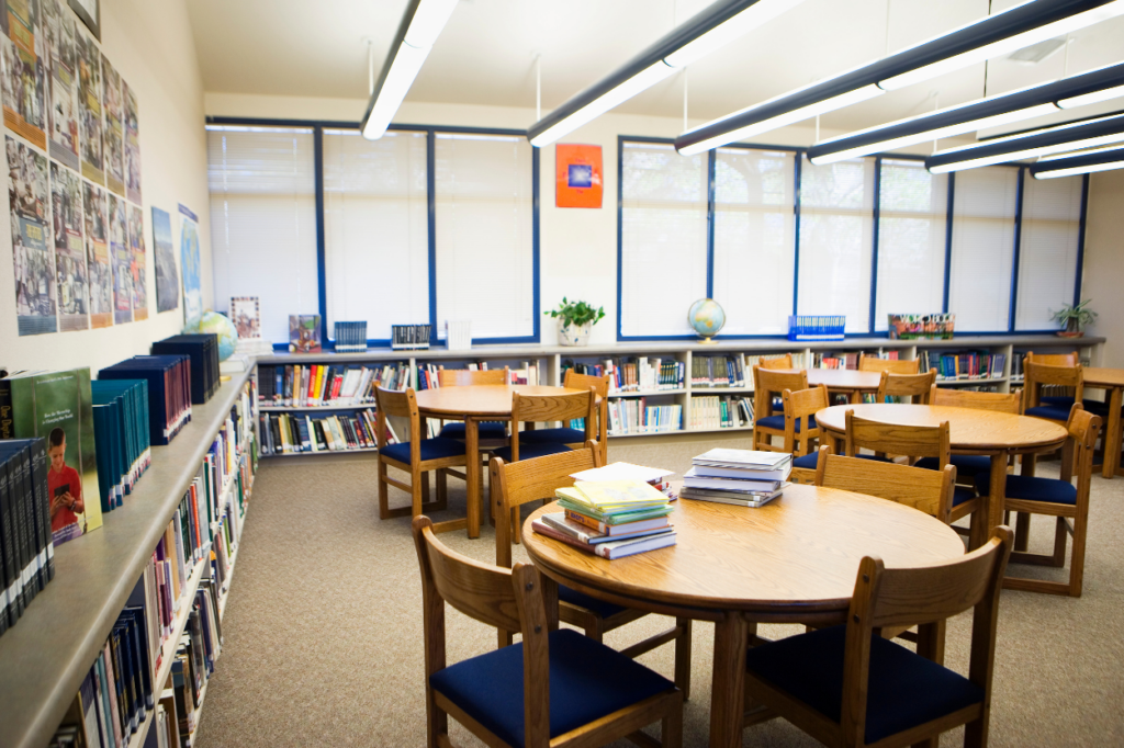 The interior of a school library with tables, chairs, shelves, and lots of books.
